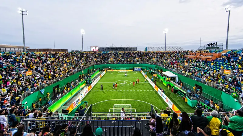 Estádio lotado durante um jogo de futebol de cegos, com a quadra no centro e a torcida nas arquibancadas.